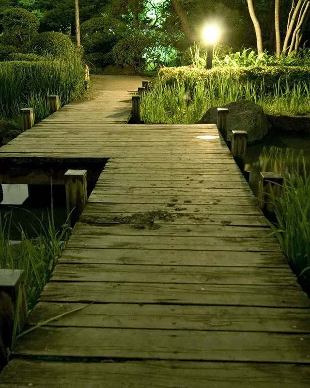 Holzsteg durch einen abendlich beleuchteten japanischen Garten